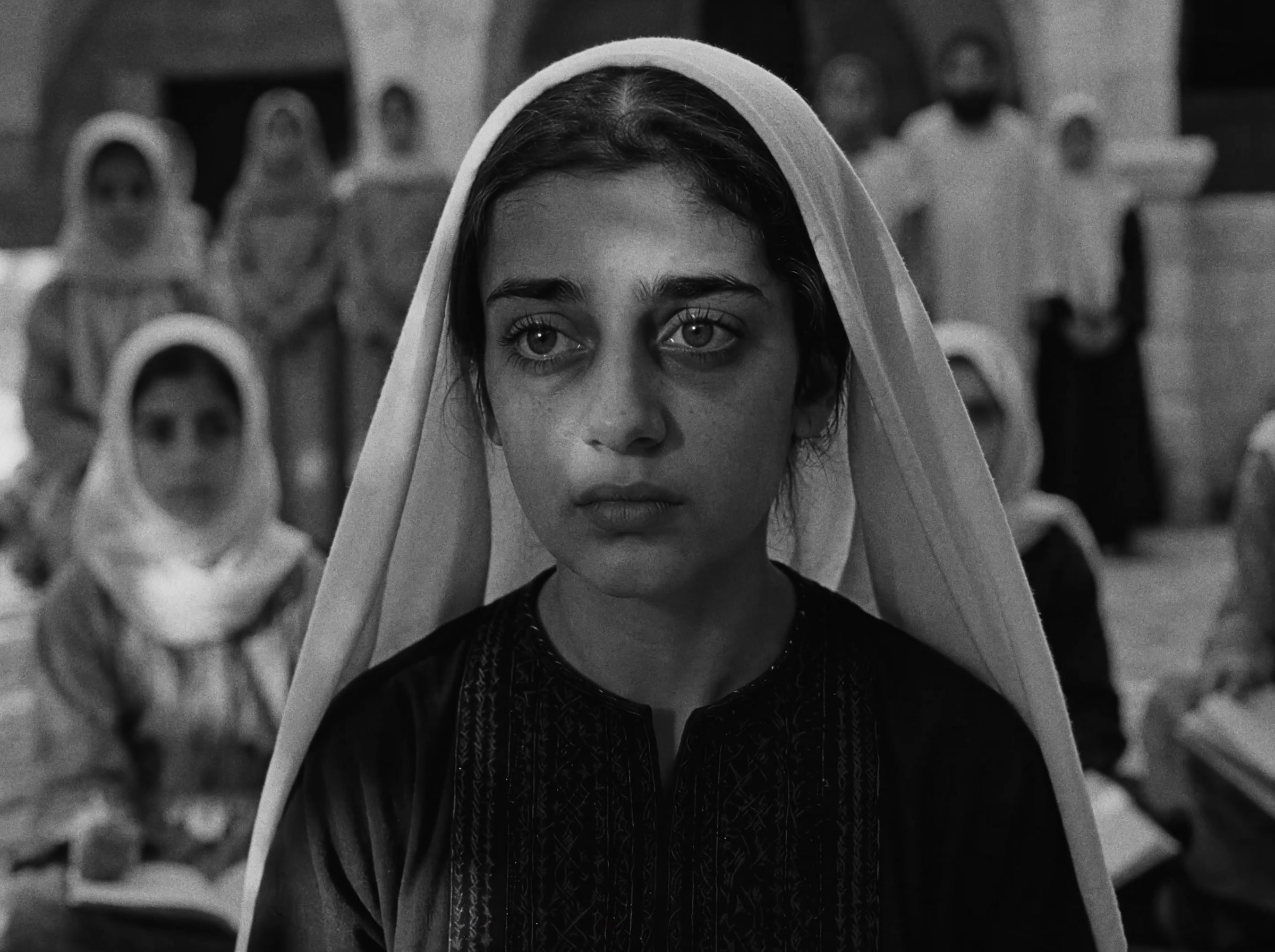 A girl in a white headscarf, other villagers behind her.