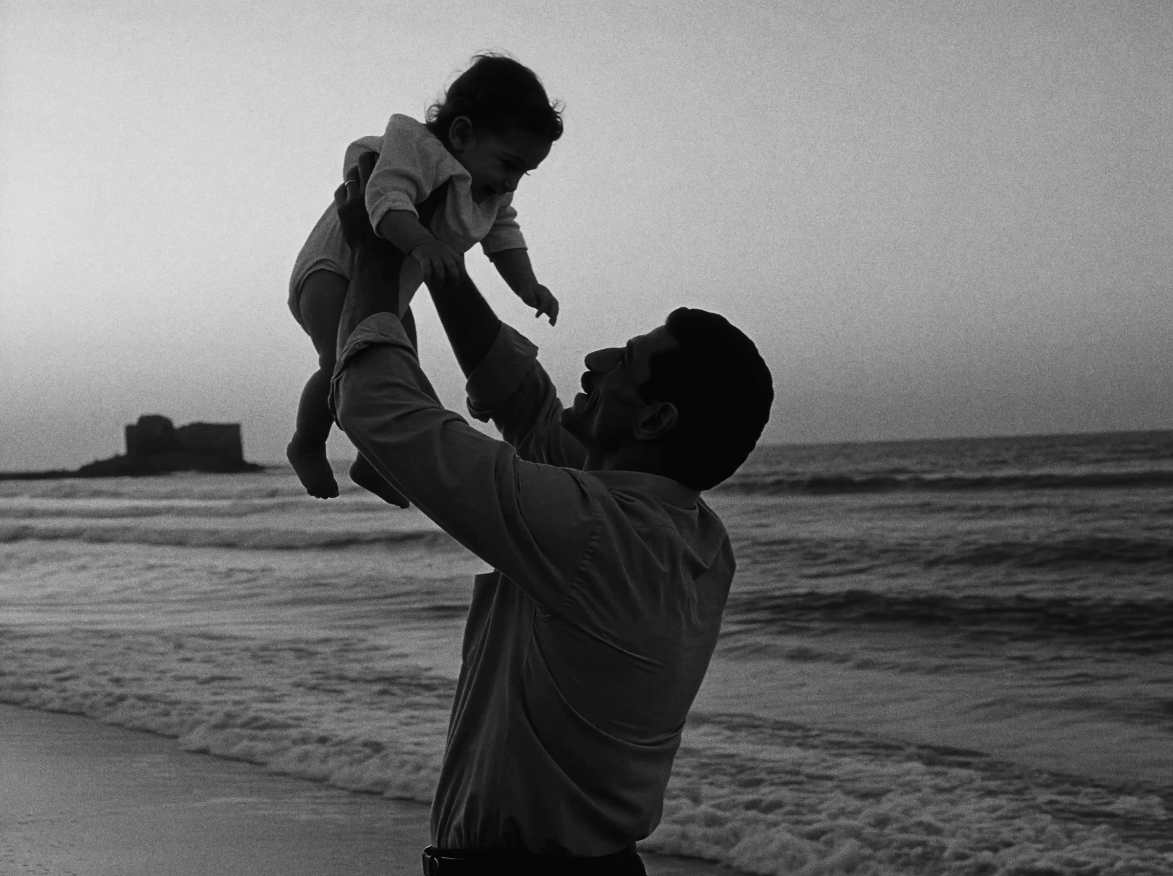 A father lifting his child above the sea.