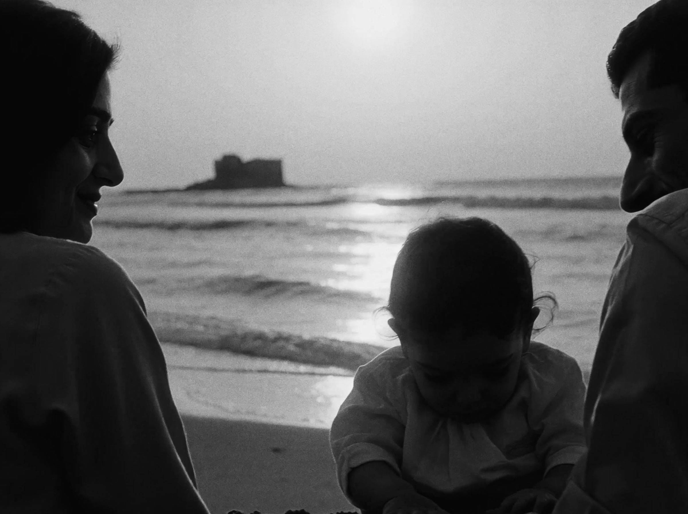 A mother, father and child on the shore at sunset.
