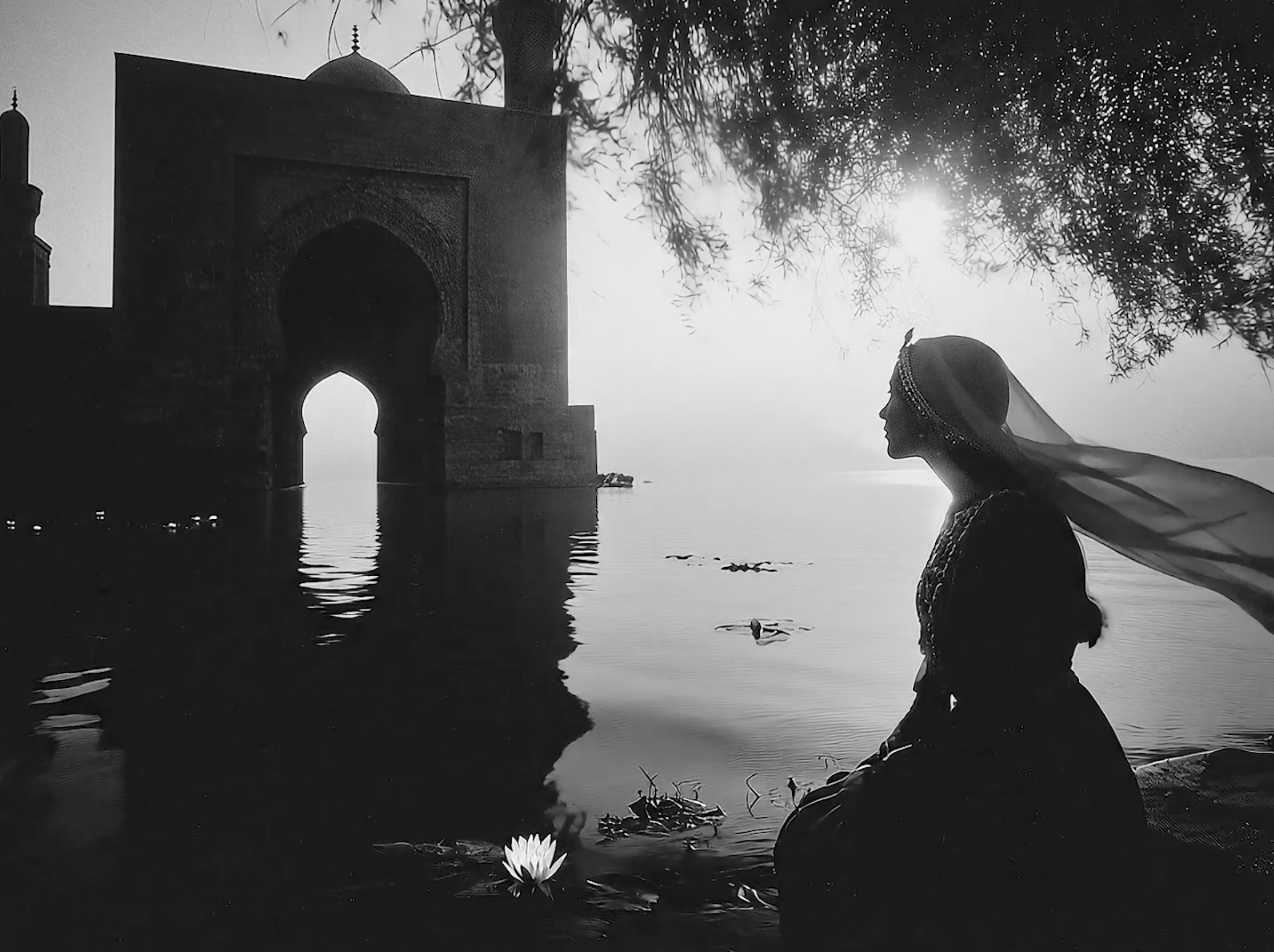A woman seated by water beneath a Moorish arch.